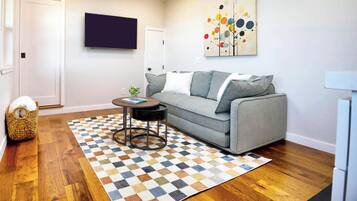 A living room with a grey sofa, a patterned rug, a small round table, and a wall-mounted TV.