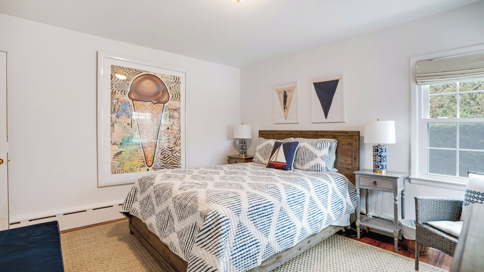 A bedroom with a bed, two nightstands, a chair, and artwork on the walls.