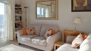 A living room with a sofa, a small table, a bookshelf, and a window with curtains.