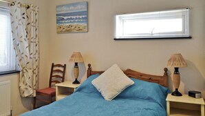 A bedroom with a bed, two bedside tables with lamps, a chair, a window with blinds, and a painting on the wall.