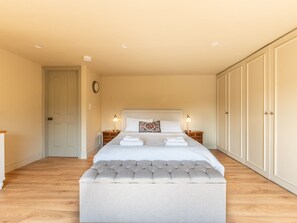 A bedroom with a large bed, two bedside tables with lamps, a tufted bench, a wardrobe, and a door. - Luxury 5-Bed Home w/ Cinema, Games Room & Garden  - Pass the Keys (London)