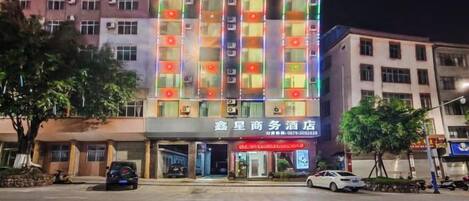 Un hotel de varios pisos con letreros iluminados, estacionamiento y vista a la calle.
