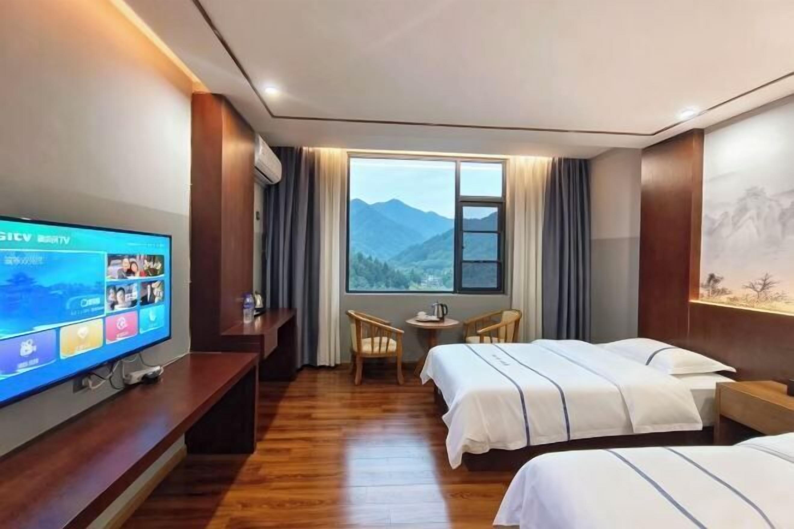 A hotel room with a TV, two beds, a desk, and a view of mountains.