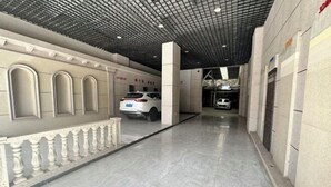 A covered walkway with a tiled floor, a white car parked on the left, and a building entrance on the right. - Mojiang XinXing Business Hotel (Mojiang)