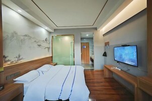 Quarto de hotel com cama, televisão, um banco de madeira e uma parede com pintura.