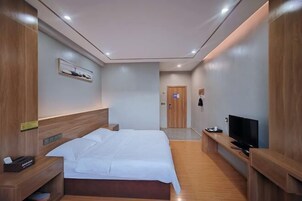 Quarto de hotel moderno com uma cama grande, cabeceira de madeira, uma TV sobre um suporte de madeira e uma pequena escrivaninha com uma luminária.