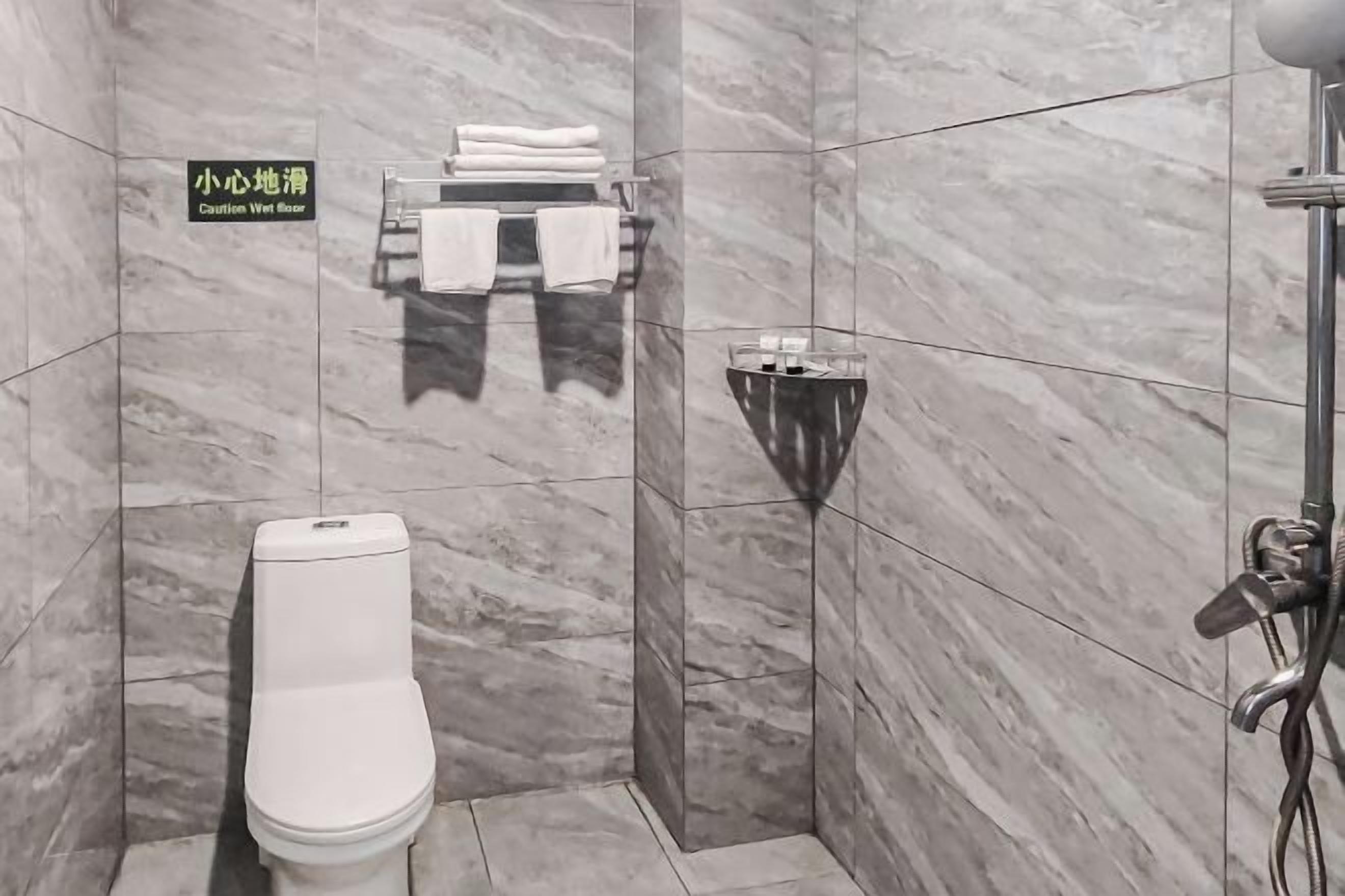 Un baño con inodoro, toallero con toallas dobladas y zona de ducha con lavamanos con mampara de vidrio.