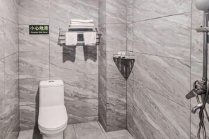 Un baño con inodoro, toallero con toallas dobladas y zona de ducha con lavamanos con mampara de vidrio.