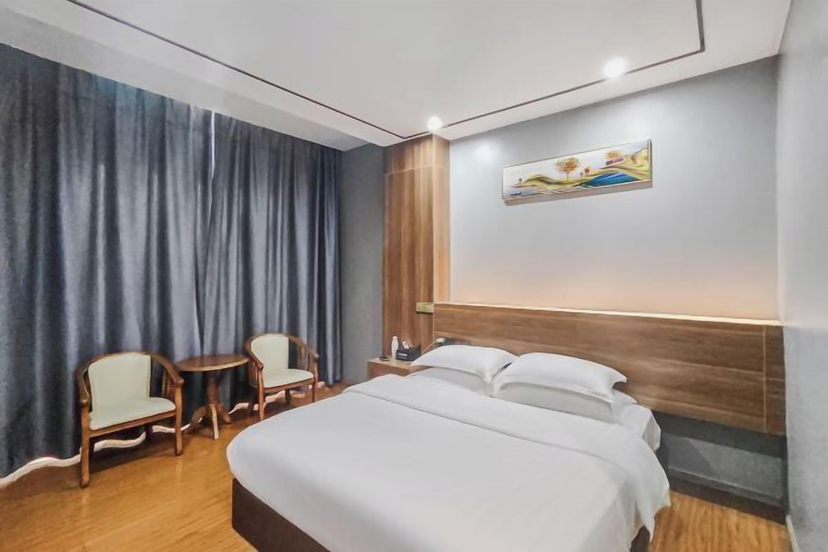 A hotel room with a large bed, two chairs, a small table, and a painting on the wall.