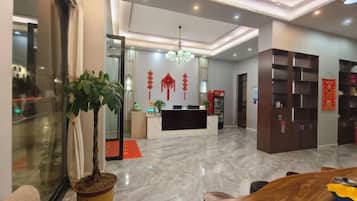 A hotel lobby with a reception desk, seating area, and a large potted plant.
