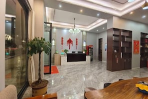 A hotel lobby with a reception desk, seating area, and a large potted plant. - Mojiang XinXing Business Hotel (Mojiang)