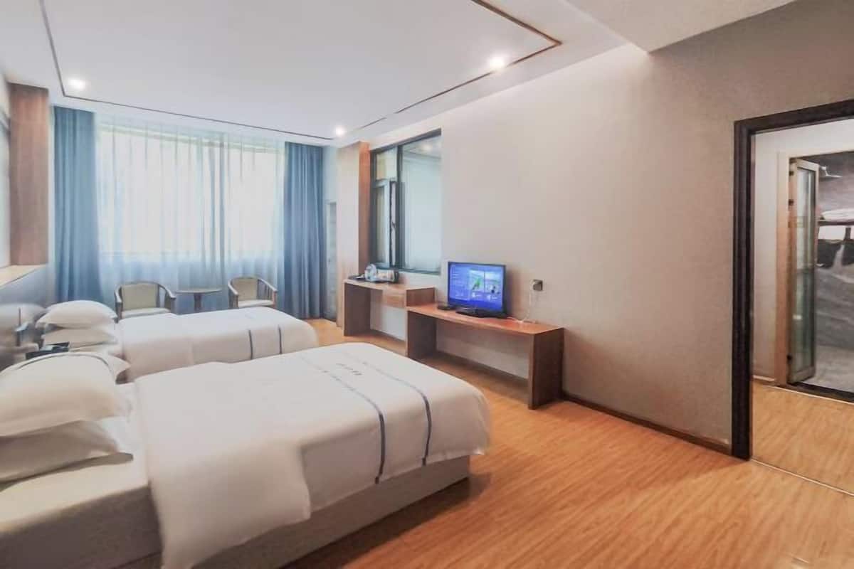 A hotel room with two beds, a TV, a desk, and a window with curtains.