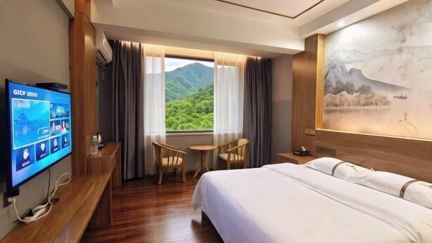 A hotel room with a bed, a desk, a chair, a TV, and a window with a mountain view. - Mojiang XinXing Business Hotel (Mojiang)
