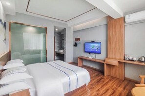 A hotel room with a bed, a TV, a wooden desk, and a wardrobe. - Mojiang XinXing Business Hotel (Mojiang)