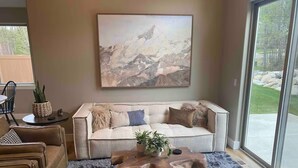 Een woonkamer met een groot raam, een bank, een bijzettafeltje en een schilderij aan de muur.