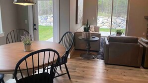 Een eethoek met een houten tafel en stoelen, een hanglamp, en uitzicht op een tuin door glazen deuren.