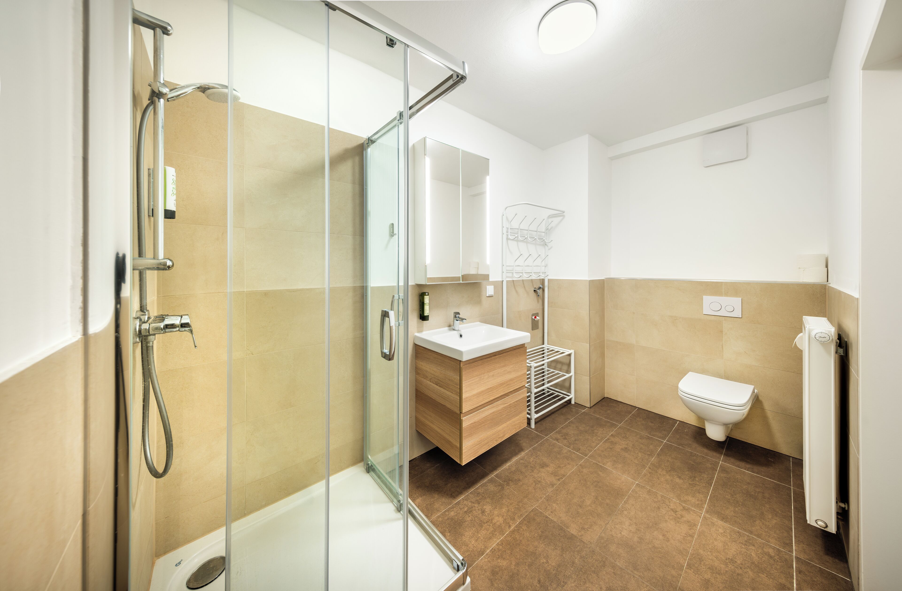 Un baño moderno con cabina de ducha de vidrio, tocador de madera, inodoro blanco y perchero para toallas.