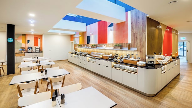 A modern dining area with a central island counter, white tables, and wooden chairs. - Jimmys Apartments XXL (Vienna)