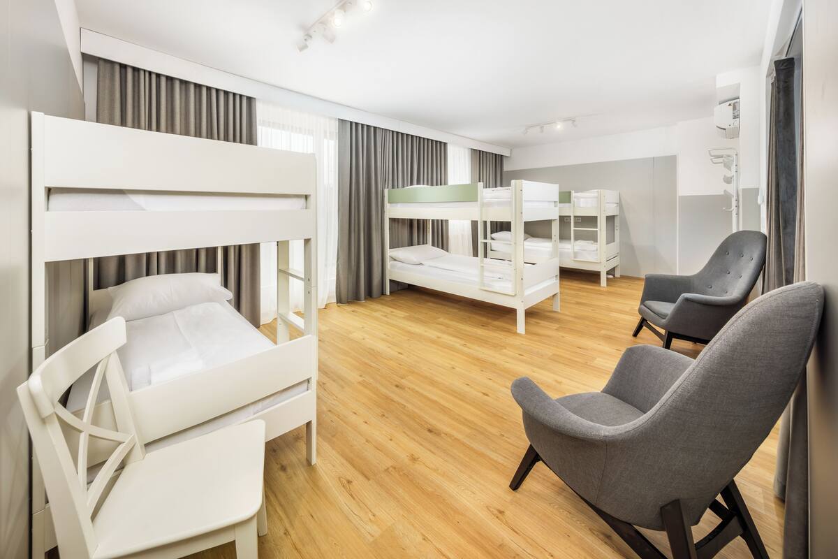 A modern hotel room with bunk beds, a desk, a chair, and a wardrobe.