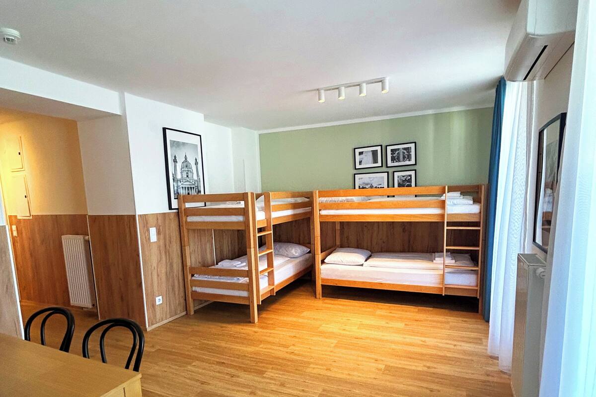 A room with bunk beds, a dining table, chairs, and a radiator.