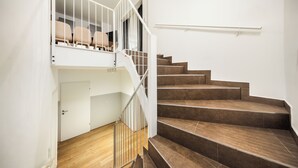 A staircase with a white railing leading to a landing with beige chairs. - Jimmys Apartments XXL (Vienna)