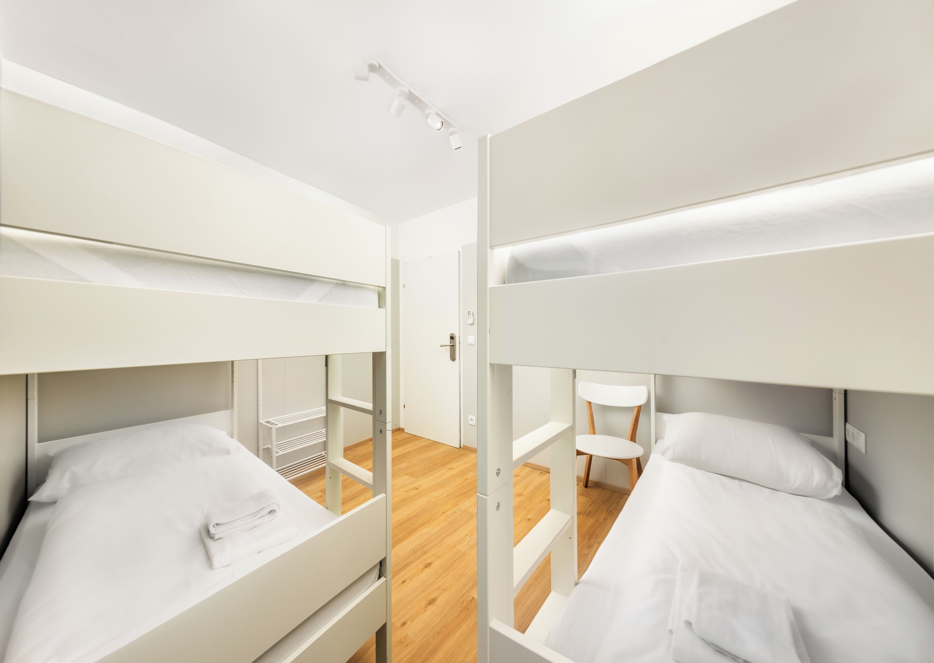 A modern, minimalist room with bunk beds, a wooden floor, and a white door.
