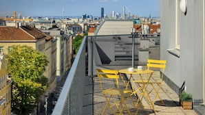 A rooftop terrace with yellow chairs and a table, overlooking a cityscape with buildings and a clear sky. - Jimmys Apartments XXL (Vienna)