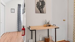 A hallway with a wooden floor, a fire extinguisher, a wall-mounted picture, and a door with a patterned curtain.