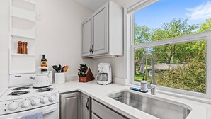 A modern kitchen with white cabinetry, a Danby stove, a coffee maker, and a large window with a view of greenery.