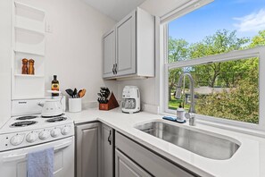 A modern kitchen with white cabinetry, a Danby stove, a coffee maker, and a sink with a view of greenery outside.