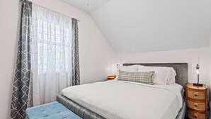 A bedroom with a bed, a bench, a bedside table, and a lamp.