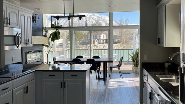 Une cuisine moderne avec des meubles blancs, un grand îlot central et une vue sur les montagnes par les fenêtres.