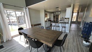 Une cuisine moderne avec des meubles blancs, un îlot central et un coin repas comprenant une table et des chaises en bois.