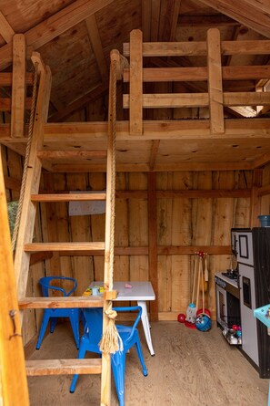 A rustic wooden interior with a lofted sleeping area, a small table with chairs, and a kitchenette.