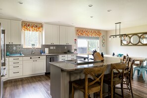 A modern kitchen with white cabinets, a central island, and a dining area with wooden chairs.