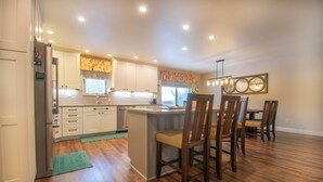 A modern kitchen with wooden flooring, white cabinets, and a central island with chairs. - Kenai Riverfront Cabin! Fish, Explore, & Relax! (Sterling)