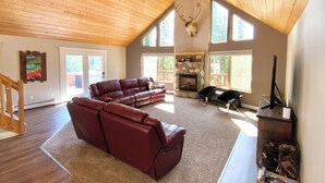 A spacious living room with a large brown leather sofa, a fireplace, and a ceiling fan. - Kenai Riverfront Cabin! Fish, Explore, & Relax! (Sterling)