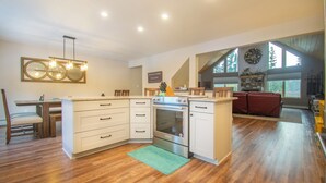 A modern kitchen with a built-in oven, white cabinetry, and a dining area with a wooden table and chairs. - Kenai Riverfront Cabin! Fish, Explore, & Relax! (Sterling)
