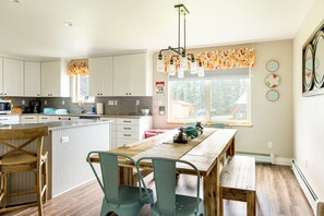 A modern kitchen with white cabinets, a wooden dining table, and a large window.