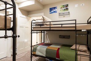 Une chambre avec un lit superposé, une porte, une étagère fixée au mur et une couvre-lit matelassé.