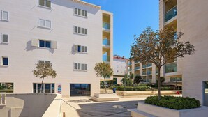 Un bâtiment moderne doté de nombreux balcons, d’une cour avec des sièges et d’un arbre.