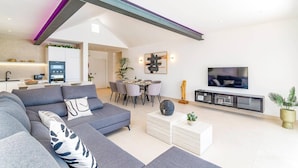En moderne stue med en grå sofa, spiseplads, et køkken og et fjernsyn.