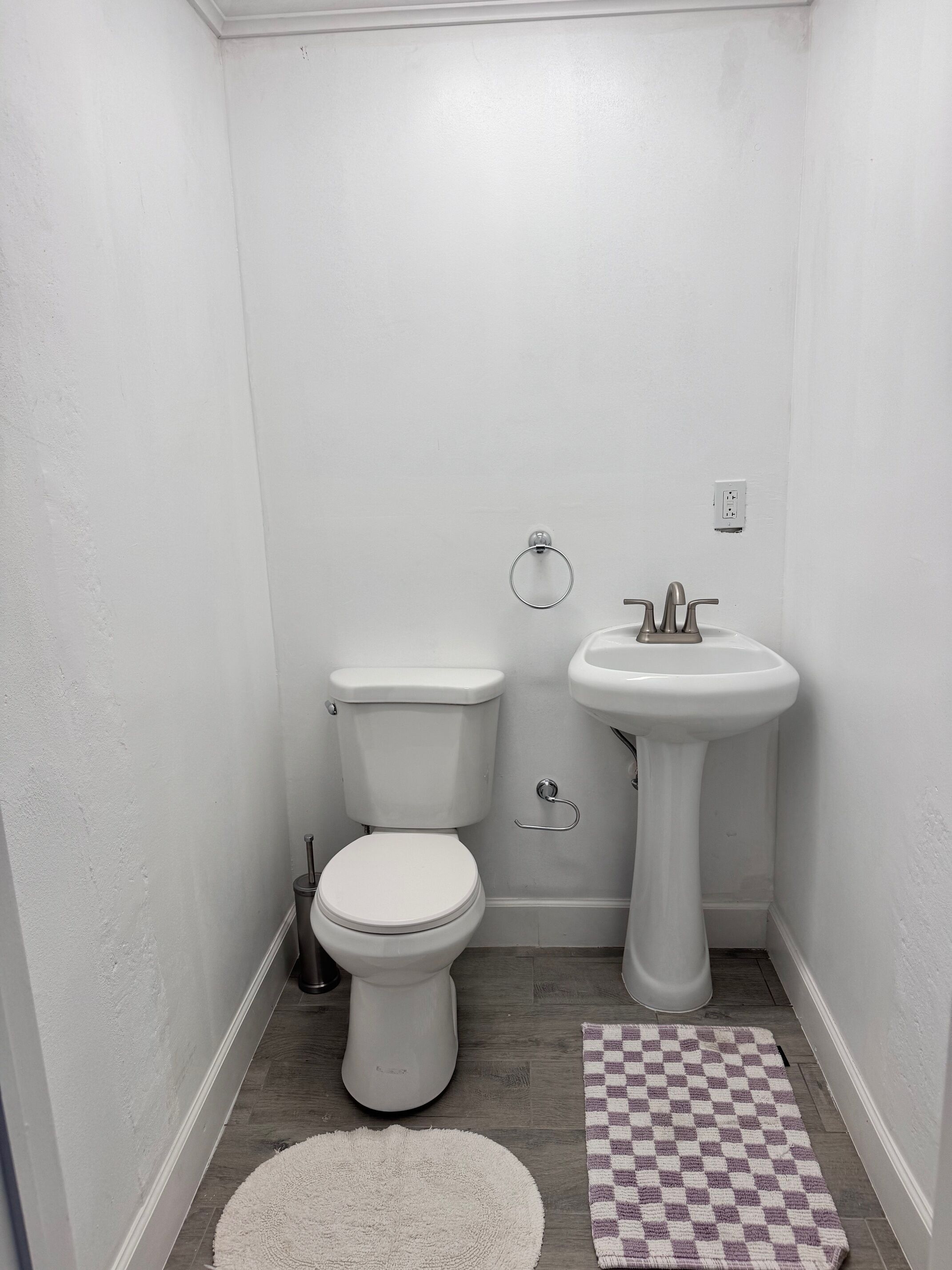 Une petite salle de bain blanche, avec des toilettes, un lavabo et un tapis à carreaux sur le sol.