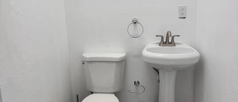 Une petite salle de bain blanche, avec des toilettes, un lavabo et un tapis à carreaux sur le sol.