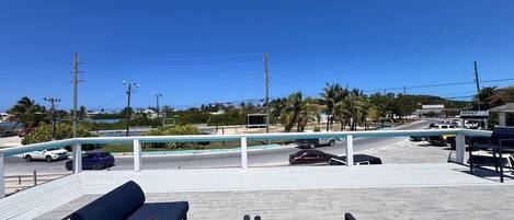 A parking area with a few cars, a bench, and a view of palm trees and buildings in the distance.