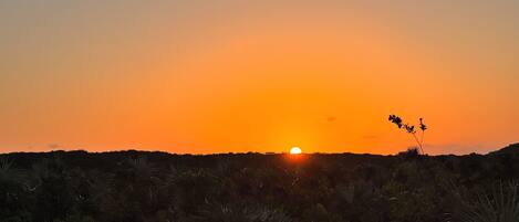 A sunset over a dry, hilly landscape with sparse vegetation.