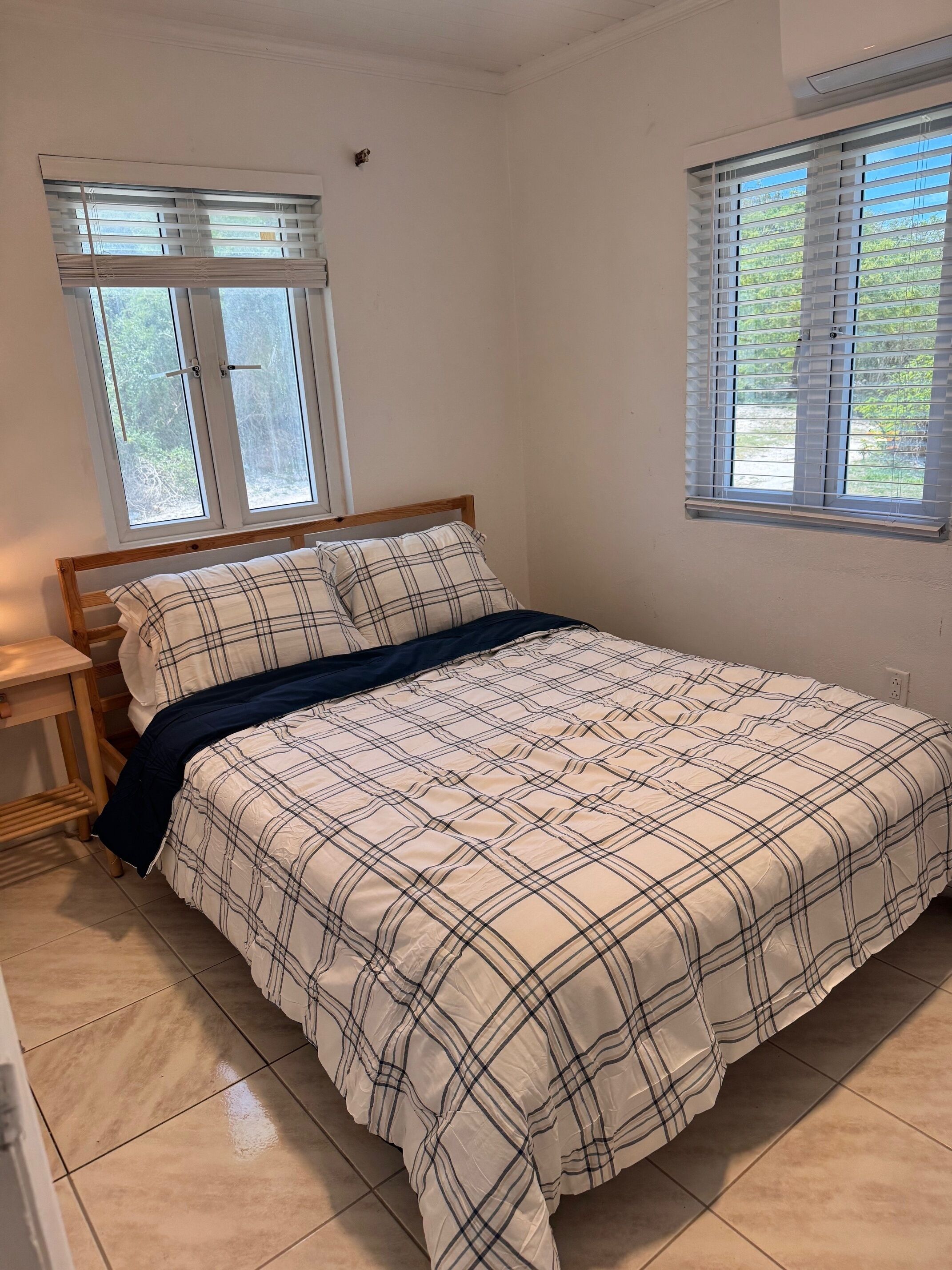 Une chambre à coucher avec un lit, deux fenêtres, une table de chevet et un radiateur fixé au mur.