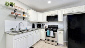 Une cuisine moderne avec des meubles blancs, une cuisinière en acier inoxydable, un réfrigérateur noir et un plan de travail en granit.