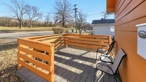 A wooden deck with a bench and a chair, a small shed, and a road in the background. - Clean, quiet 2BR home with utilities included and fast WiFi. Comfortable setup with open surroundings and easy access to downtown Kansas City (about 15 minutes). Ideal for short stays, work trips, or a simple, reliable place to unwind. (Sugar Creek)
