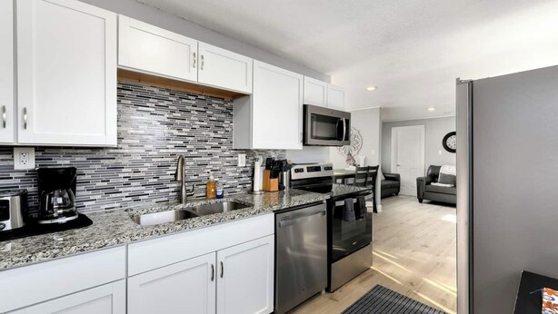 A modern kitchen with white cabinets, a granite countertop, stainless steel appliances, and a backsplash with a mosaic tile pattern. - Clean, quiet 2BR home with utilities included and fast WiFi. Comfortable setup with open surroundings and easy access to downtown Kansas City (about 15 minutes). Ideal for short stays, work trips, or a simple, reliable place to unwind. (Sugar Creek)